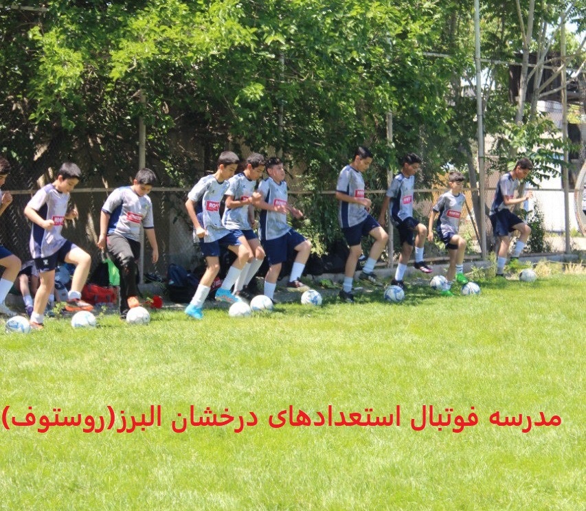 فوتبالیستهای نوجوان با لباسهای طوسی سورمه ای در زمین چمن طبیعی در حال آموزش فوتبال
