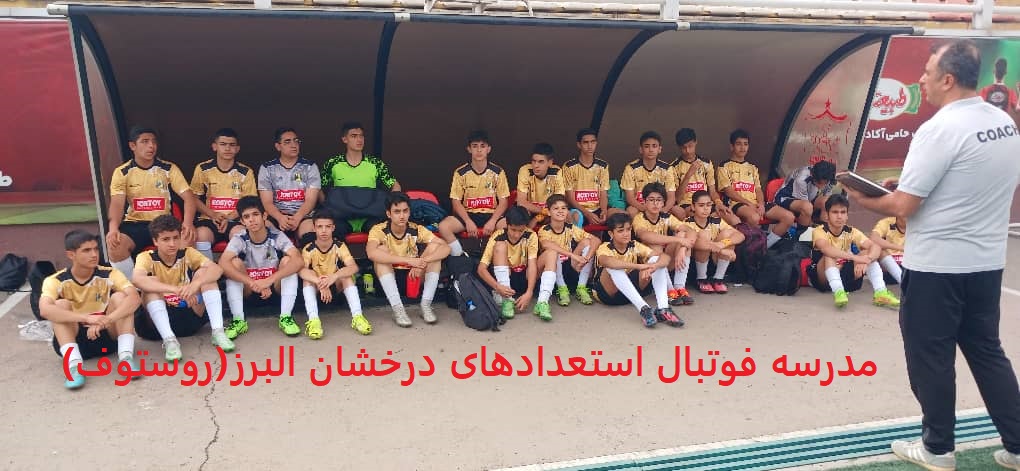 فوتبالیستهای نوجوان با لباسهای طلایی مشکی نشسته روی نیمکت کنار زمین چمن فوتبال و گوش دادن به صحبتهای مربی خود