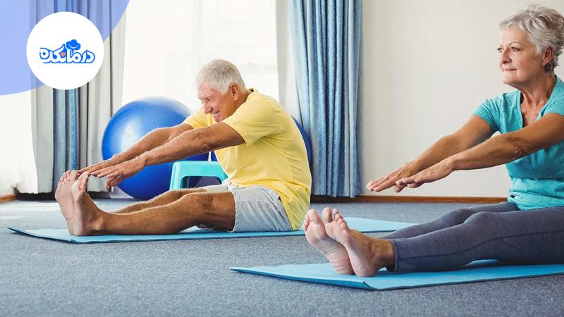 تصویر خانم و آقای سالمندی را نشان می‌دهد که در حال انجام حرکات کششی ورزشی روی مت هستند.