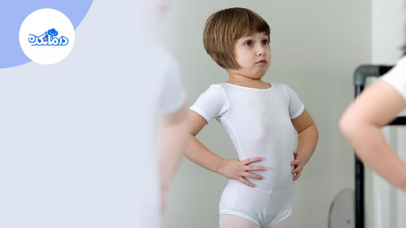 دختر بچه‌ایی که لباس سفید ژیمناستیک پوشیده است. او دست‌هایش را به کمر زده و جلوی آینه به اندام خود نگاه می‌کند.