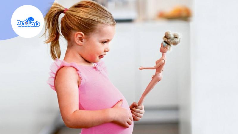دختر بچه‌ایی که عروسک باربی در دست دارد و در حال تماشای اوست.