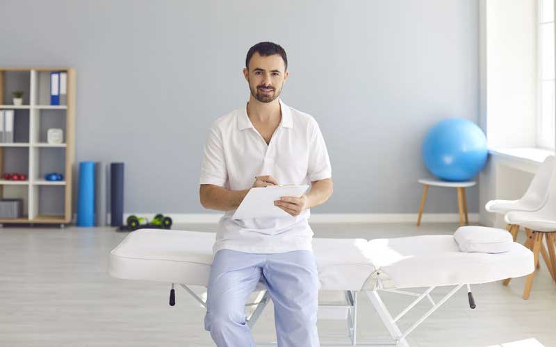 تصویر ماساژ درمانگر مرد در کنار تخت ماساژ در خانه