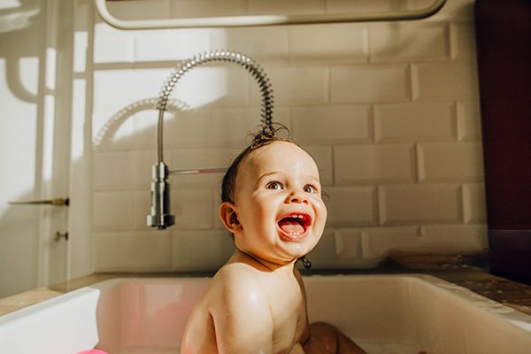 کودک خندان مشغول آب بازی در زیر شیر ظرفشویی فنری